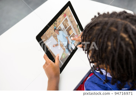 Mixed race schoolboy using digital tablet on video call with male teacher 94716971