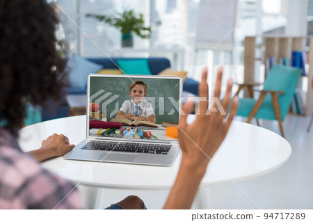 Mixed race female teacher using laptop and waving on video call with schoolboy Mixed race female teacher using laptop and waving on video call with schoolboy 94717289
