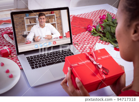Diverse couple making valentine's date video call using laptop both holding gifts Diverse couple making valentine's date video call using laptop both holding gifts 94717318