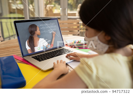 Caucasian schoolgirl wearing face mask and using laptop on video call with female teacher Caucasian schoolgirl wearing face mask and using laptop on video call with female teacher 94717322
