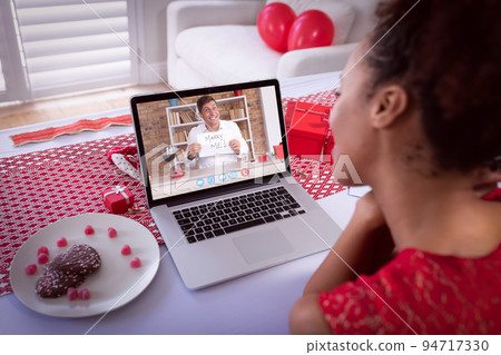 Diverse couple making valentine's date video call the man on laptop screen holding marry me sign Diverse couple making valentine's date video call the man on laptop screen holding marry me sign 94717330