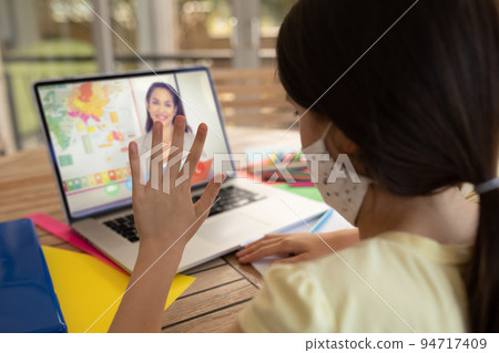 Caucasian schoolgirl wearing face mask, using laptop and waving on video call with female teacher 94717409