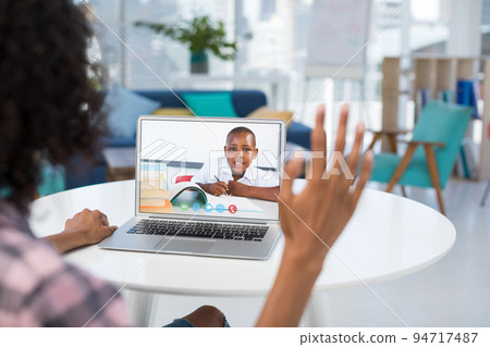 Mixed race female teacher using laptop and waving on video call with schoolboy 94717487