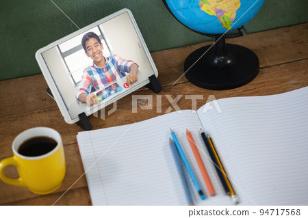 Mixed race schoolboy learning on tablet screen on desk during video call 94717568