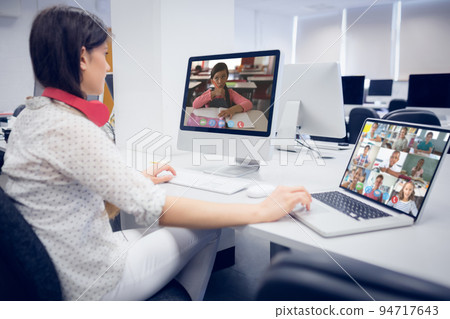Caucasian female teacher using computer and laptop on video call with school children 94717643
