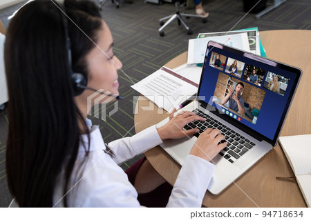 Caucasian woman in office having video call with colleagues displayed on laptop screen Caucasian woman in office having video call with colleagues displayed on laptop screen 94718634