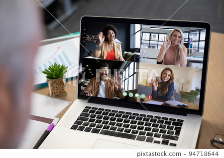Diverse business people waving displayed on laptop screen during office video call 94718644