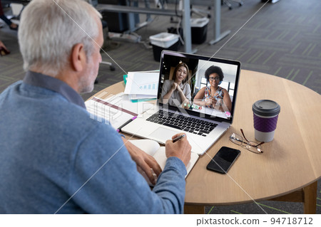 Caucasian man in office having video call with colleagues displayed on laptop screen Caucasian man in office having video call with colleagues displayed on laptop screen 94718712