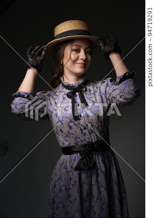 A beautiful woman in a romantic dress of the 19th century. Retro style, with a straw hat and lace gloves. Historical reconstruction. Romantic lady countess in a dark room. High quality photo A beautiful woman in a romantic dress of the 19th century. Retro style, with a straw hat and lace gloves. Historical reconstruction. Romantic lady countess in a dark room. High quality photo 94719291