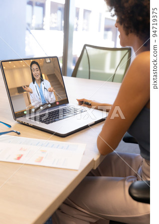 Biracial woman with curly hair talking with asian female doctor on videocall over laptop Biracial woman with curly hair talking with asian female doctor on videocall over laptop 94719375