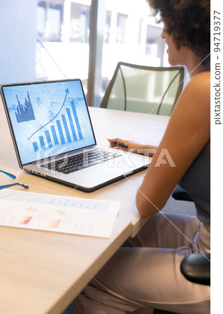 African american businesswoman analyzing growth report over laptop on desk at office African american businesswoman analyzing growth report over laptop on desk at office 94719377
