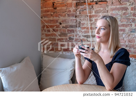 Beautiful smiling woman drinking coffee at cafe. Portrait of young blonde woman in a cafe drinking Beautiful smiling woman drinking coffee at cafe. Portrait of young blonde woman in a cafe drinking 94721032