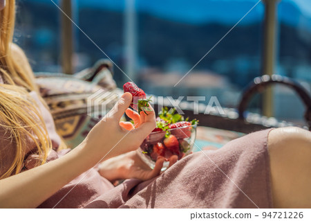 Portrait of gorgeous woman wearing beautiful dress sitting in a patio and eating strawberry 94721226