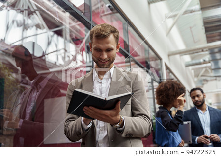 Businessman looks into notepad while standing in office against background of colleagues  94722325