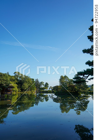 A beautiful view of clear blue sky and trees reflected on the water surface of Kasumigaike Pond in Kenrokuen in the morning｜Kanazawa City, Ishikawa Prefecture 94722958