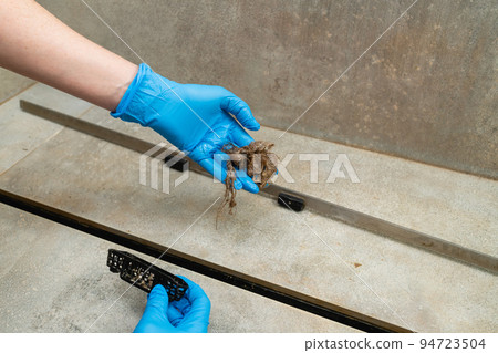 Woman removing hair clump from the shower drain. 94723504
