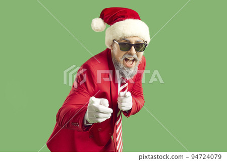 Happy funny man in red suit, Christmas hat and cool sunglasses points finger at you 94724079