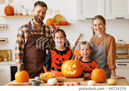 Happy family mother, father and kids looking at camera, make jack-o-lantern from pumpkin, getting ready for halloween Happy family mother, father and kids looking at camera, make jack-o-lantern from pumpkin, getting ready for halloween 94724159