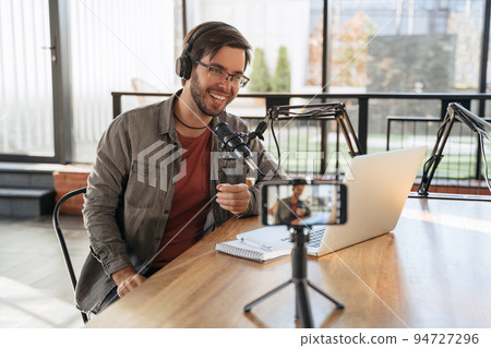 Man podcaster in headphones recording video podcast on smartphone 94727296