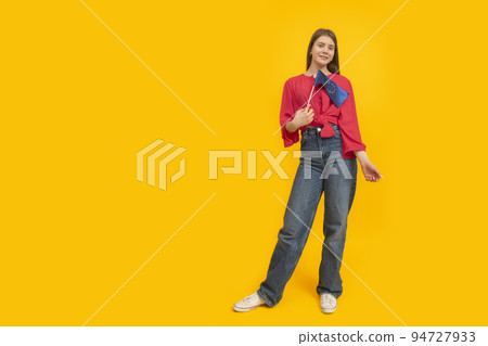 Full-length portrait of young girl with the EU flag in her hands on yellow background. Study in Europe. Space for text 94727933