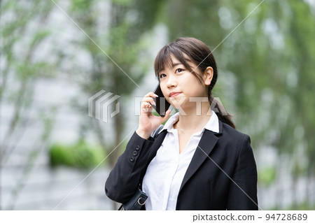 Young woman in suit using smartphone outdoors 94728689