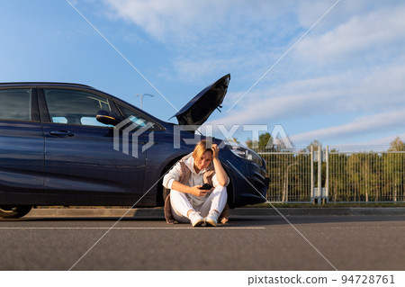woman driver waiting for help from emergency tow truck near broken down car with open hood 94728761