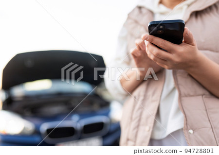 photo with depth of field, focus on mobile phone, a woman on the road next to a broken car is 94728801