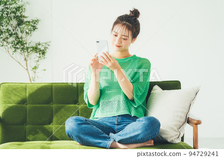 Woman sitting on a sofa and looking at a smartphone 94729241
