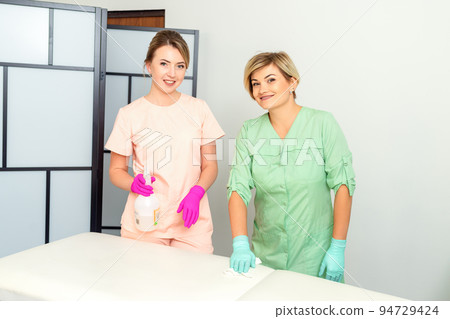 Two medical workers disinfect the patient's couch with sanitizer spray and a clean napkin. Health and hygiene concept Two medical workers disinfect the patient's couch with sanitizer spray and a clean napkin. Health and hygiene concept 94729424