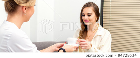 The female cosmetologist doctor treats his patient to a cup of coffee in a medical office The female cosmetologist doctor treats his patient to a cup of coffee in a medical office 94729534