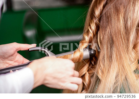 The female hairdresser is curling hair for a brown-haired young caucasian woman in a beauty salon The female hairdresser is curling hair for a brown-haired young caucasian woman in a beauty salon 94729536