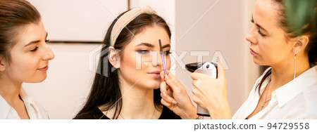 Makeup artist using an airbrush on the face of a young caucasian woman in a beauty salon Makeup artist using an airbrush on the face of a young caucasian woman in a beauty salon 94729558