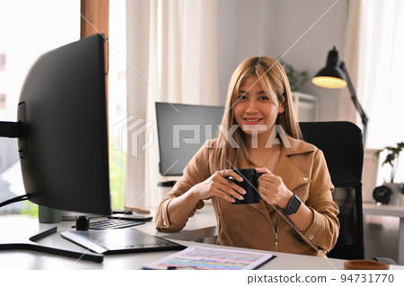 Attractive young creative woman sitting front of professional computer in her home office and smiling to camera Attractive young creative woman sitting front of professional computer in her home office and smiling to camera 94731770