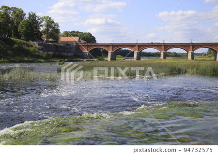 View from the waterfall to the ancient arched brick bridge and old city. High quality photo View from the waterfall to the ancient arched brick bridge and old city. High quality photo 94732575