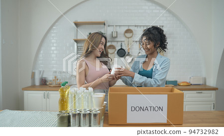 Volunteer concept of 4k Resolution. Asian women packing food in a donation box together at home. Consumer goods donated to help the victims. 94732982