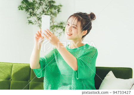Woman sitting on a sofa and looking at a smartphone Woman sitting on a sofa and looking at a smartphone 94733427