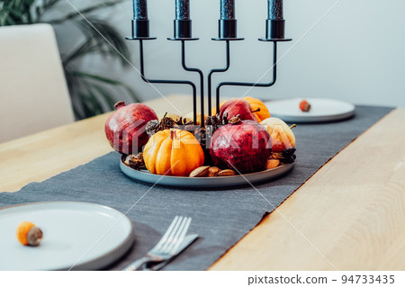 Fall table setting for romantic celebration Thanksgiving day for two. Autumn composition with candles, pumpkins ,pomegranates, fruits and cones. Natural autumn decor. Selective focus 94733435