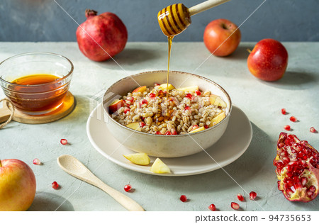Sweet homemade barley porridge with pomegranate seeds, apples and honey. Rosh Hashanah celebration Sweet homemade barley porridge with pomegranate seeds, apples and honey. Rosh Hashanah celebration 94735653