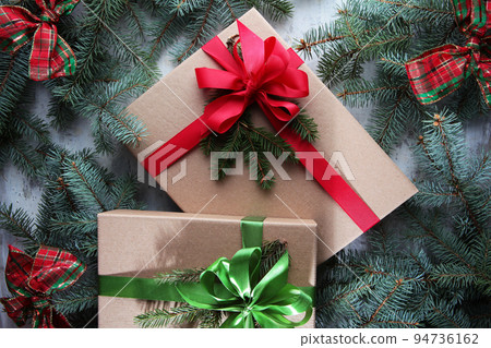 Two boxes with a gift for the New Year. The lids of the boxes are tied with green and red satin ribbons. New Year or Christmas. Branches of a coniferous tree. Flat lay.Top view. 94736162