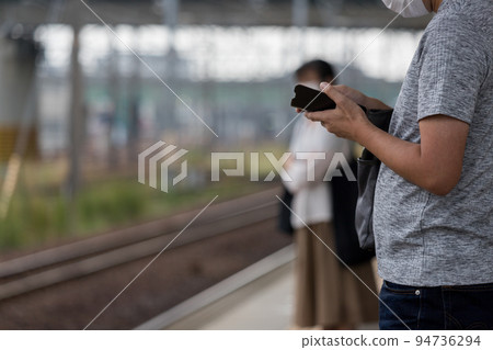 Back view of a man operating a smartphone on the station platform 94736294