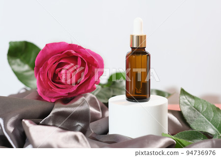 Product for skincare based on rose oil, essential oil solution ina dropper bottle, brown pipette bottle and fresh pink rose flower next to silk textile cloth. Product for skincare based on rose oil, essential oil solution ina dropper bottle, brown pipette bottle and fresh pink rose flower next to silk textile cloth. 94736976