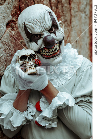 creepy evil clown holds a skull in his hands 94737912