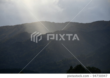 Landscape on a cloudy day with light visible from the sky towards the mountains Landscape on a cloudy day with light visible from the sky towards the mountains 94738947