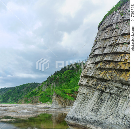 coastal landscape, beautiful columnar basalt cliff on the wooded coast of Kunashir island coastal landscape, beautiful columnar basalt cliff on the wooded coast of Kunashir island 94739768