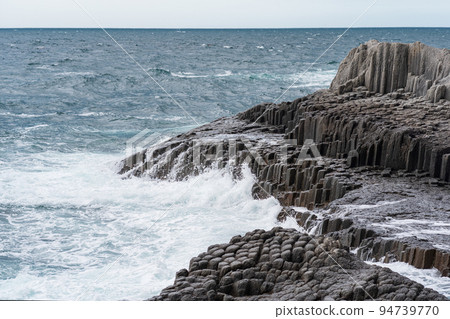 rocky seashore formed by columnar basalt against the backdrop of a stormy sea, coastal landscape of the Kuril Islands rocky seashore formed by columnar basalt against the backdrop of a stormy sea, coastal landscape of the Kuril Islands 94739770