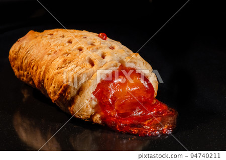 Baked bun with red strawberry jam in electric oven: close up, black background 94740211
