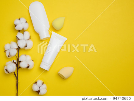 White plastic tubes  and jar for cream, gel and other cosmetics and sponges on a yellow background, top view 94740690