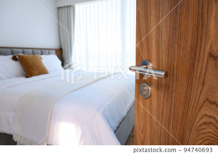 wooden door open to modern bedroom. selective focus to door handle, bedroom blurred on background. Hotel room, Condominium, or apartment doorway. 94740693