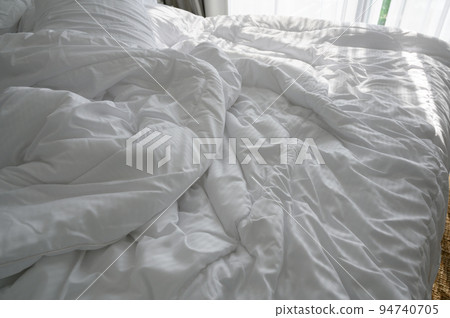 Messed bedroom in the morning. Rumpled bed with white blanket and messy pillow decoration in bedroom. 94740705