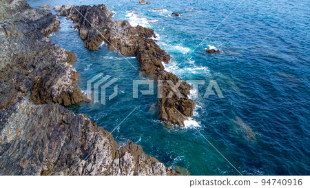 Beautiful waves break on the coastal rocks. White foam on turquoise water. Seascape on a sunny day, top view. 94740916